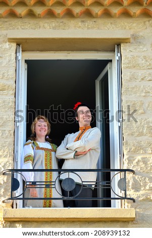 Happy young couple having fun on the balcony their house. Young man and beautiful girl in traditional russian clothes.
