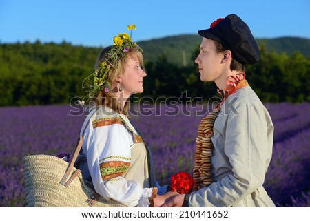 Happy young  loving couple of peasants in a lavender field at sunset light. Young man and beautiful girl in traditional russian clothes.