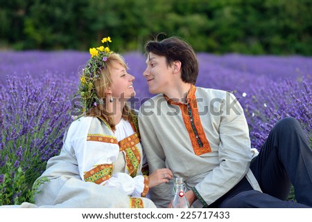 Happy young couple in a lavender field at evening time. Young man and beautiful girl in traditional russian clothes.