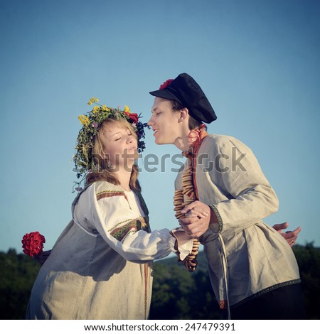 Happy young  loving couple of peasants kissing  in a lavender field at sunset light. Young man and beautiful girl in traditional russian clothes. Filtered image, vintage effect applied