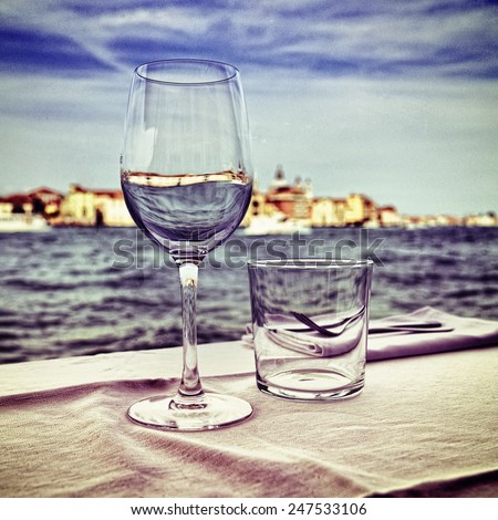 Street cafe in Venice. Empty wine glass on the table against Giudecca canal, Italy. Filtered image, vintage effect applied