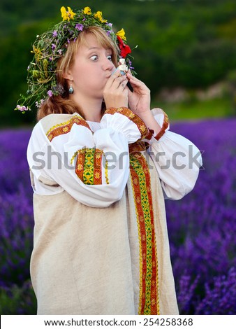 Funny peasant girl with eyes wide in russian national dress blows the whistle toy