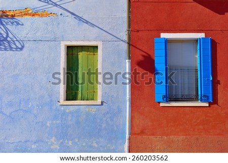 Burano island, Venice. Windows with color shutter on vivid plastered facade at sunset light. Colorful houses island and landmark of Veneto region, Italy