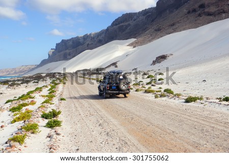 YEMEN - MARCH 11, 2010: Off-road car on the road along ocean shore with big white sand dune, Socotra island. Off-road safari is one of the main local tourist attraction in Socotra