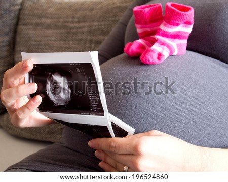 Woman looking ultrasound image of baby with baby socks on belly