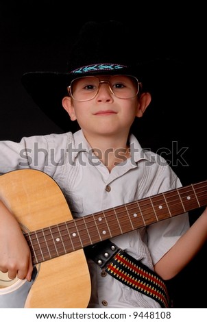 Young boy wearing a cowboy hat isolated on black playing the guitar