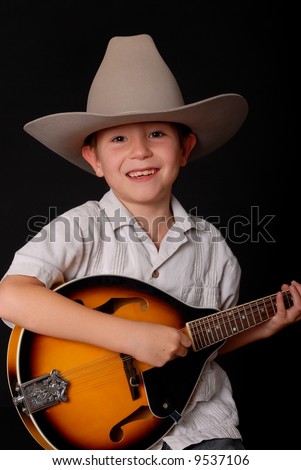 Young boy wearing a cowboy hat isolated on black playing the mandolin