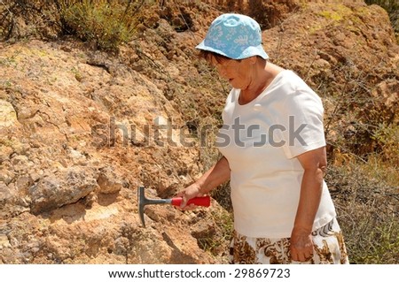 Senior woman geologist tap a rock formation with a hammer