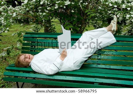Elderly woman with a illustrated, magazine in hands.   Rests on a bench in a garden. Smiles and looks in a photographic camera