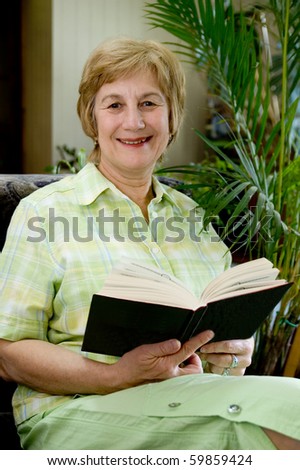 Elderly woman with a book in hands in a winter garden. Smiles and looks in a photographic camera