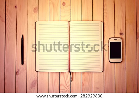 White cell phone, pen and notebook on wooden table. Work space.