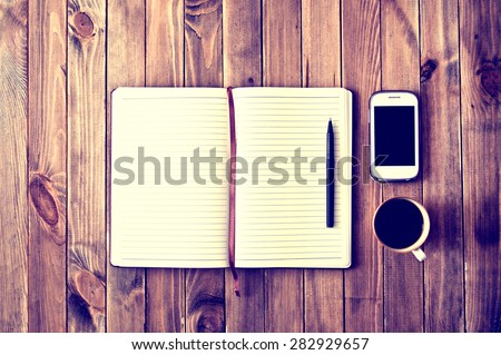 White cell phone, pen, cup of coffee and notebook on wooden table. Work space. Instagram vintage picture.