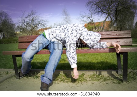 A drunken man lying on a park bench.