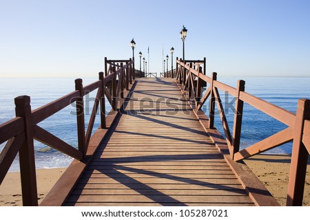 Wooden pier in good condition with barriers and lanterns on a calm Mediterranean Sea in Marbella, Costa del Sol, Andalusia, Spain.