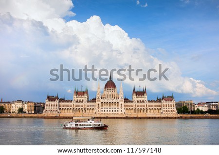 Parliament building in Budapest, Hungary, Danube river with passenger boat and dramatic sky.