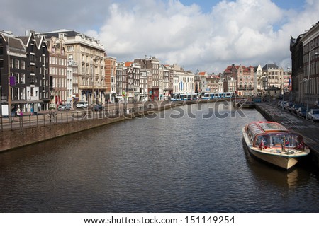 Historic buildings along Rokin street, cruise boat and pier on a canal in Amsterdam, Holland, Netherlands.