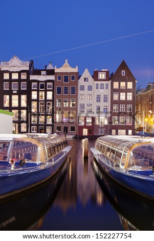 City of Amsterdam historic canal houses at night with passenger tour boats on the first plan, Netherlands, North Holland.