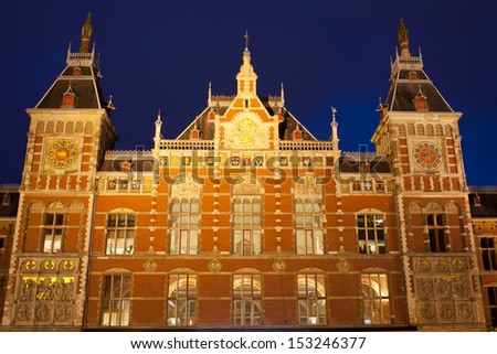 Amsterdam Central Train Station facade illuminated at night in Holland, Netherlands, city landmark from 19th century.