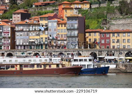 Historic houses and passenger boats docked at Douro river waterfront in the city of Porto in Portugal.