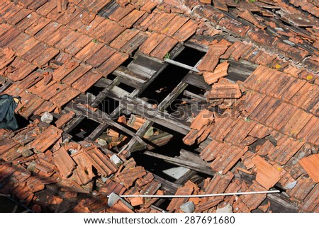 Hole in damaged clay tiled roof with wooden frame of a traditional building.