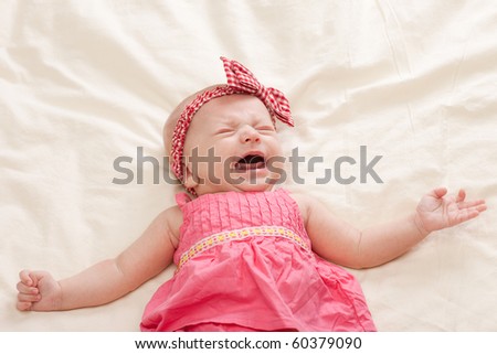 Crying and gesturing ten weeks old baby girl on bed