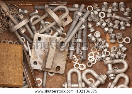 Assorted metal hardware for maintenance work consisting of a randomly scattered pile of nuts, bolts, washers and a staple