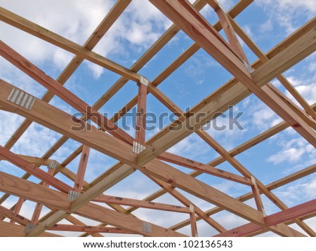 Roof frame under construction showing the wooden joists, trusses and beams against a cloudy blue sky
