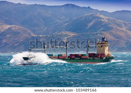 Loaded container freighter ship sailing in stormy ocean with tall and heavy breakers still near shore
