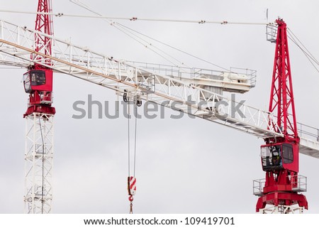 Detail of two large steel construction cranes with red operator cabs for hoisting heavy loads during building construction and development