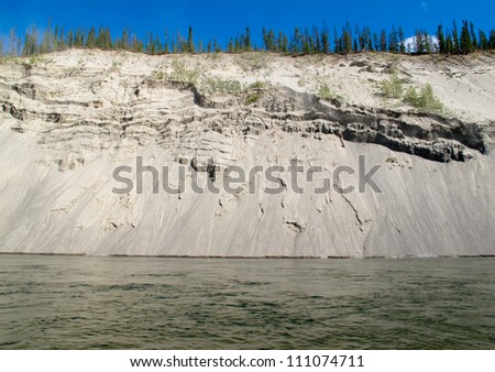 High cut bank of silt, sand and gravel slowly eroding by flowing water of mighty Yukon River, Yukon Territory, Canada