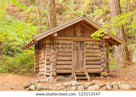 Old solid log cabin shelter hidden among green trees in the forest