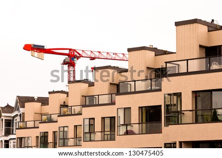 Tower crane over external facade of contemporary residential apartment block development with large glass windows and balconies for every unit.