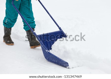 Manual snow removal from driveway using a snow scoop by person wearing boots
