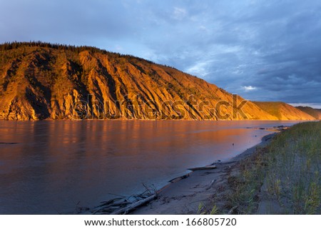Eroded clay cliff river bank at Yukon River, Yukon Territory, Canada, near Dawson City glowing in orange light of summer sunset sun