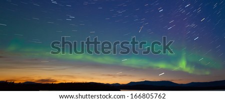 Northern lights  Aurora borealis and shooting star meteor at midnight in summer over northern horizon of Lake Laberge  Yukon Territory  Canada  at early dawn