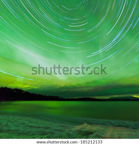 Astrophotography star trails with green sparkling show of Aurora borealis or Northern Lights over boreal forest taiga winter scene of Lake Laberge, Yukon Territory, Canada