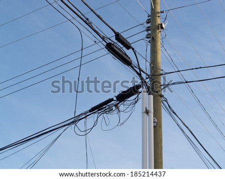 Wooden pole hung with confusing and messed-up electricity power cables and telephone lines for residential utilities supply