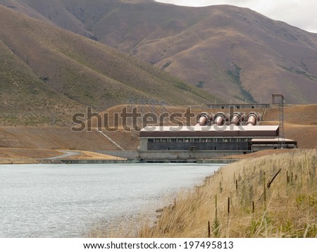 Hydroelectric power plant generator house on barren hillside with electric transmission line pylons