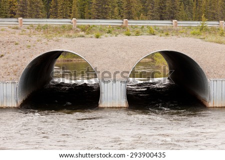 Road over dual culvert pipe infrastructure bridge strong current flow of river water tunnel through