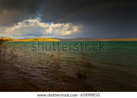 A Thundershower producing a rainbow over the gree-blue waters of pristine Lake Laberge, Yukon Territory, Canada.