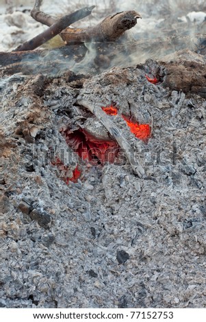 Red-hot coals still glowing and smoking under heap of ashes left from wood burning bonfire.