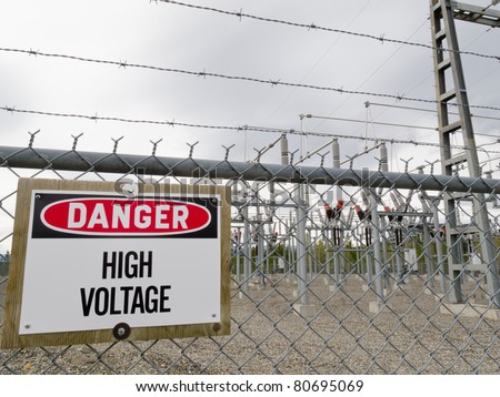 High-voltage transformer substation behind barbed-wire chain-link fence with Danger High Voltage sign.