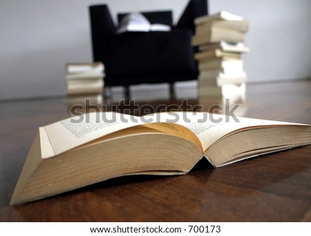 Open book in front of a chair packed with more books.