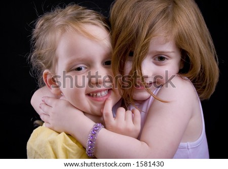 Two little girls hugging, with a kiss from the big sister.