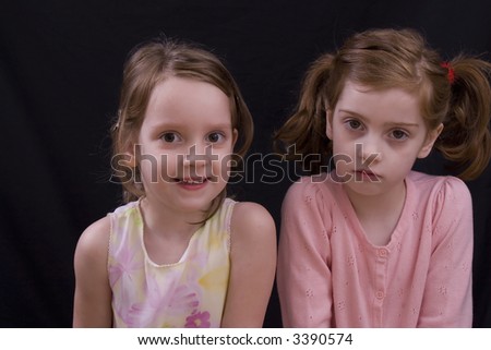 Little four and five year-old sisters on a black background.
