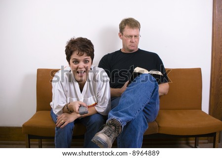 Husband and wife sitting on a retro couch with the woman watching tv and the man reading a book.