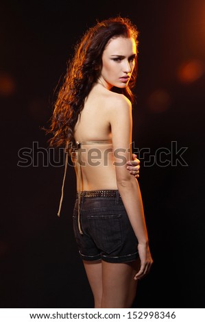 Portrait of beautiful girl in a bathing golden suit in shorts, posing on black background
