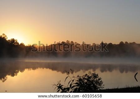 orange sunrise reflects forest terrain on foggy lake