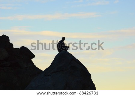 Meditating man sitting on top of a rock in the mountains