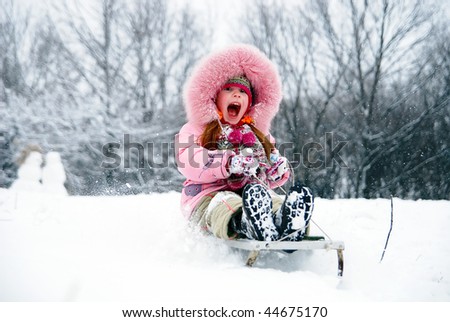little girl in winter clothing goes down on sleds down the hill